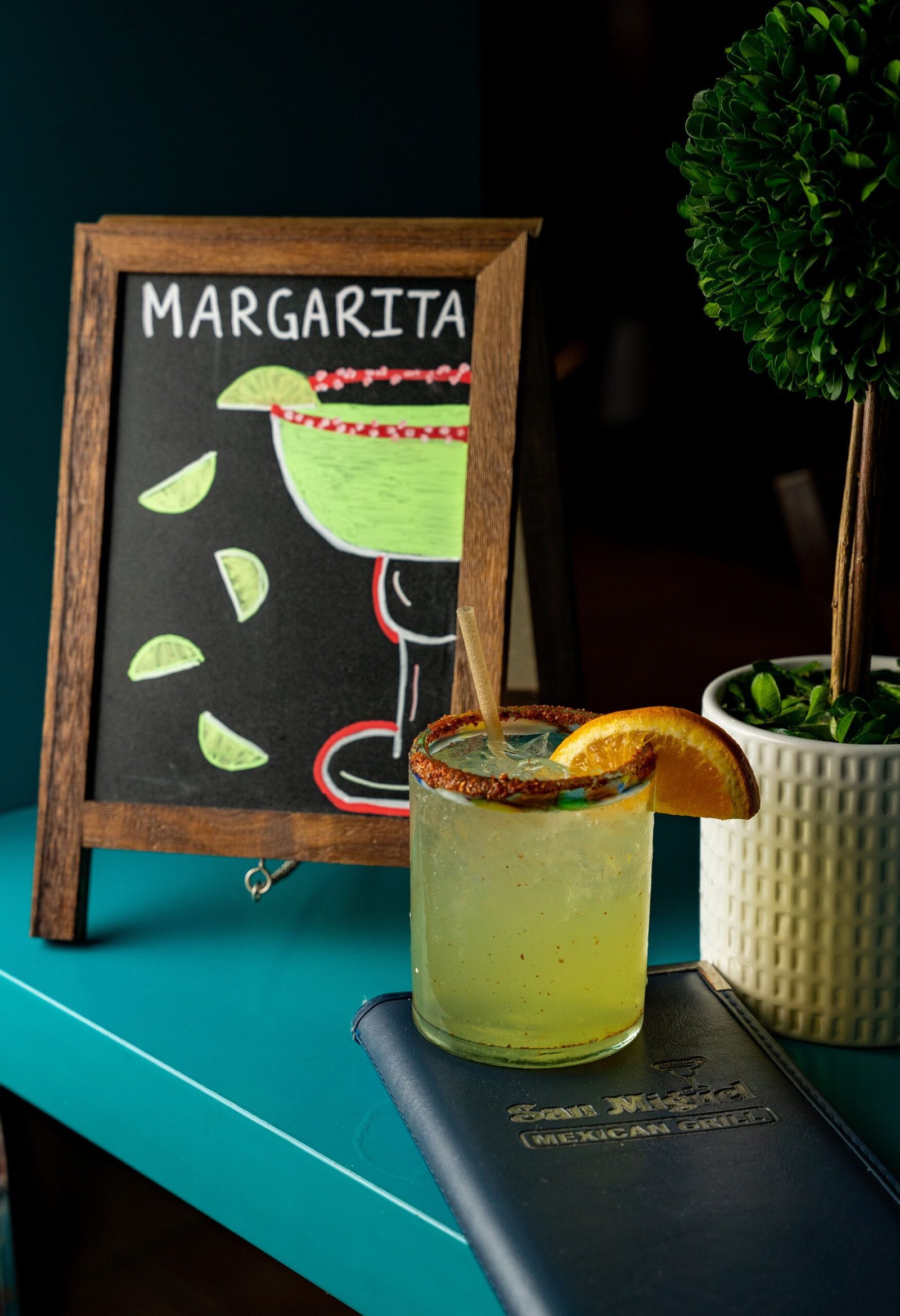 Vibrant margarita cocktail with orange slice garnish in cozy bar setting.